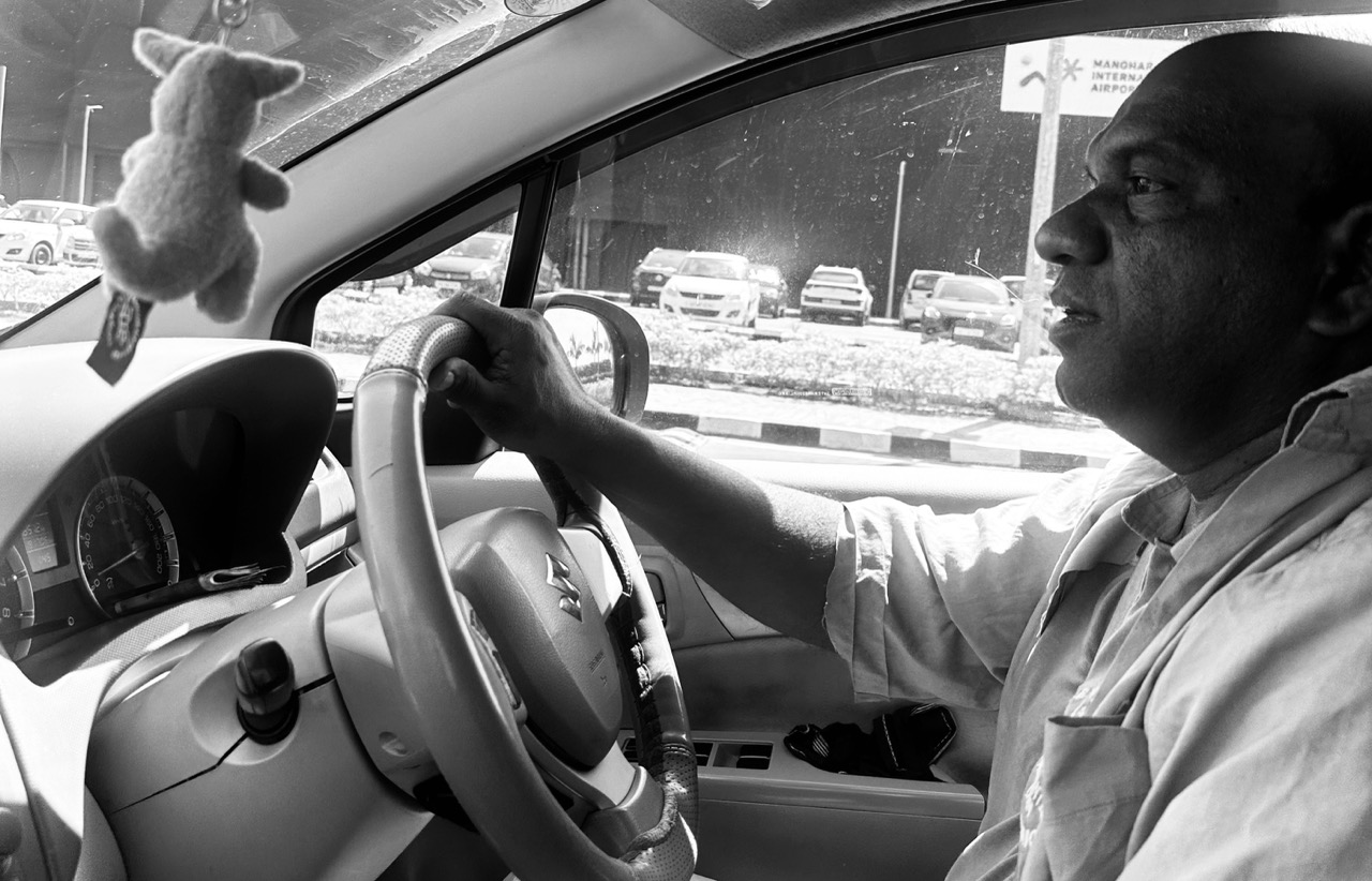 A black-and-white photo of Anand driving. The Goa airport is seen in the background.