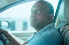 A photo of Anand driving the car, shot on film. The highway to Goa Mopa airport is seen in the background. Shot with Rollei 35S on Kodak Pro Image 100 film.
