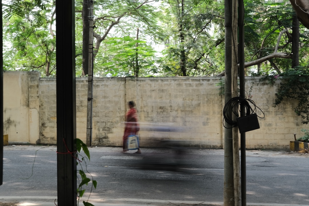 A blurred figure of a woman walking quickly down the tree-lined street
