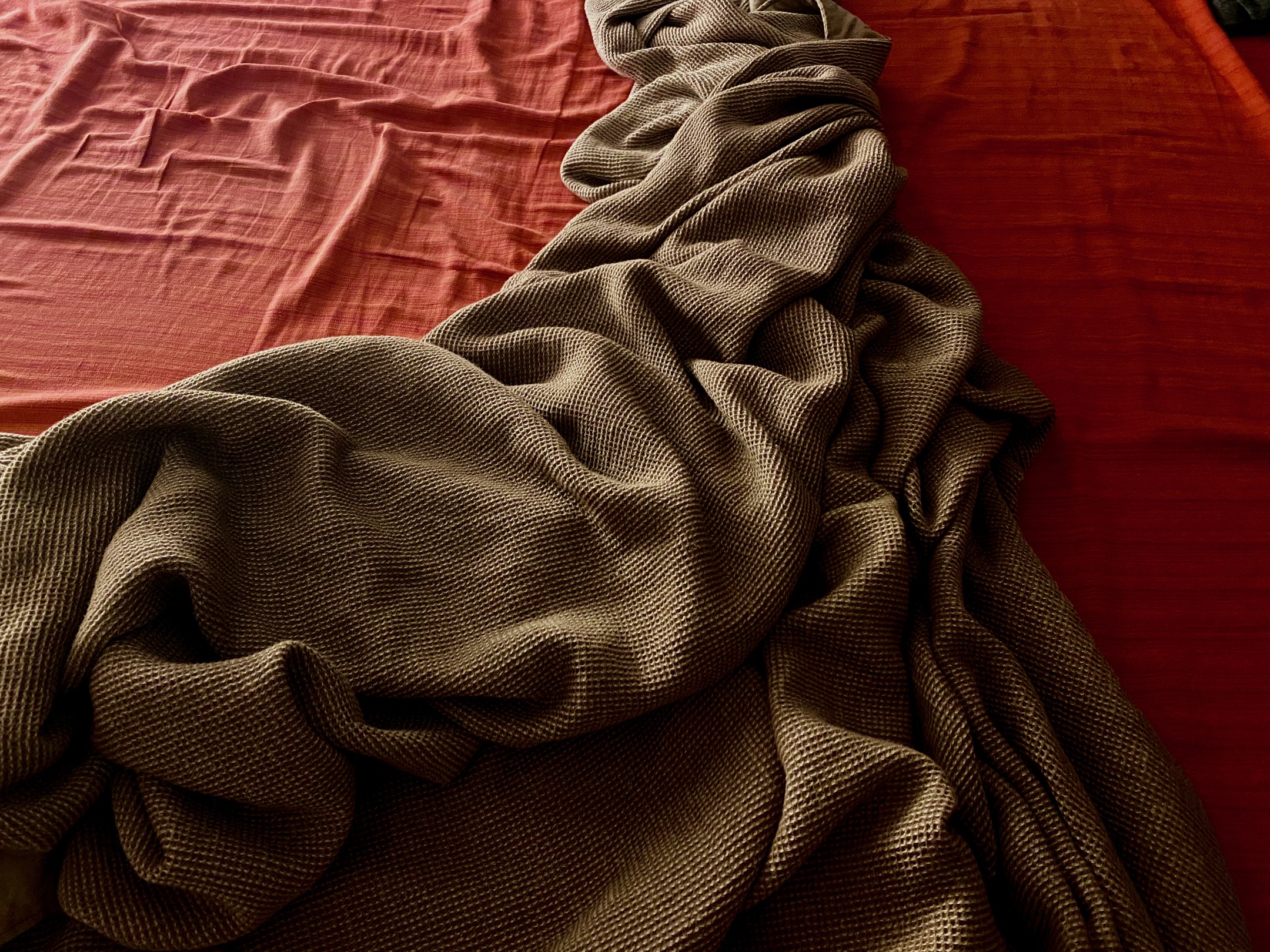 An earthen blanket with pitted texture thrown on a bed with a brick colored bedspread.