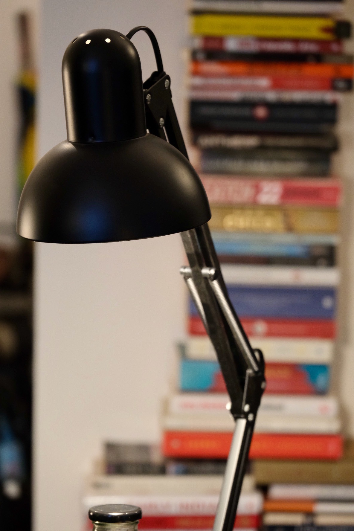 A swing-arm lamp shown in close-up with a pile of books in the background.