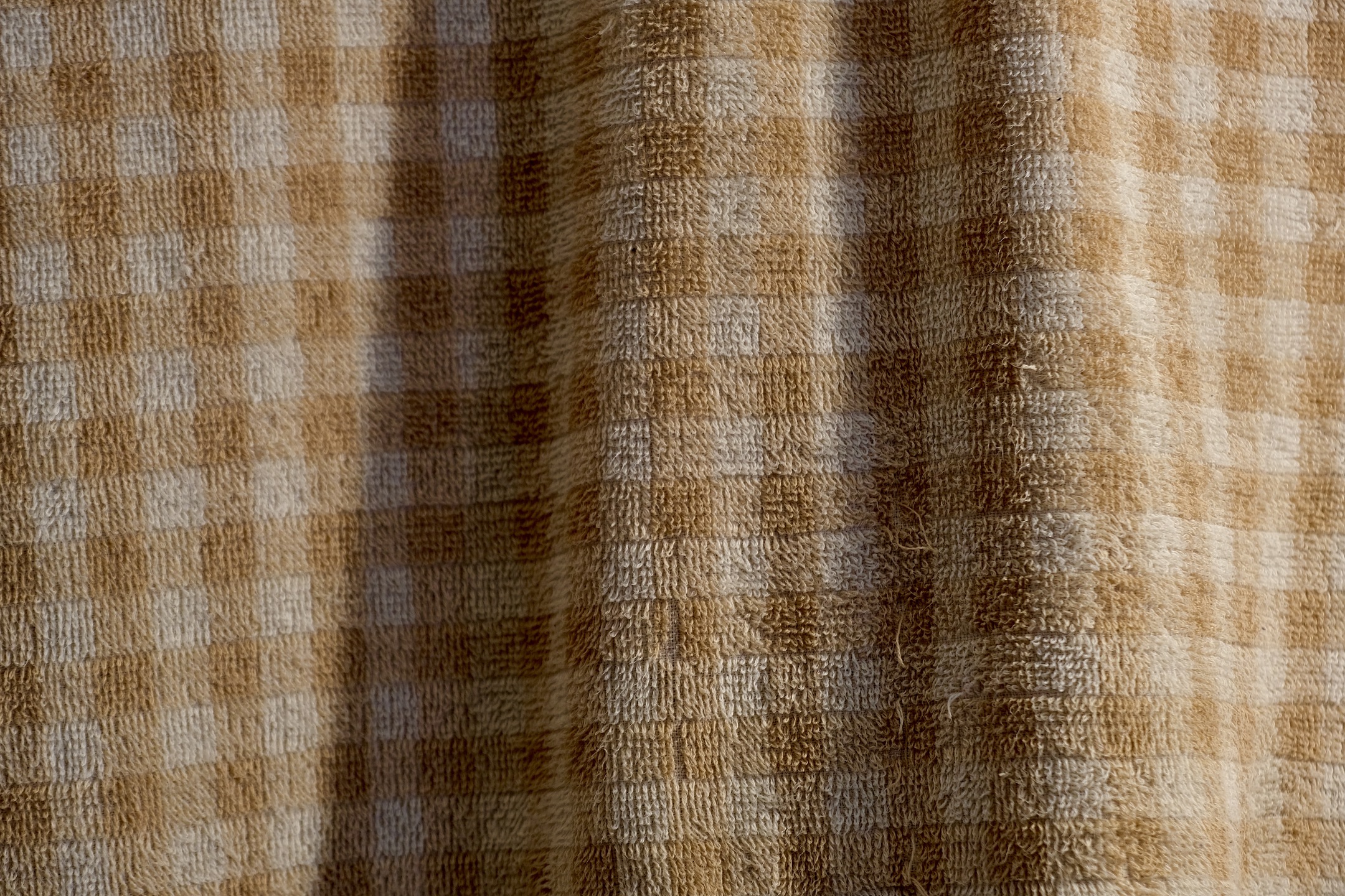 A towel with white and off-white checkered pattern hanging with slight frills—forming shadows.