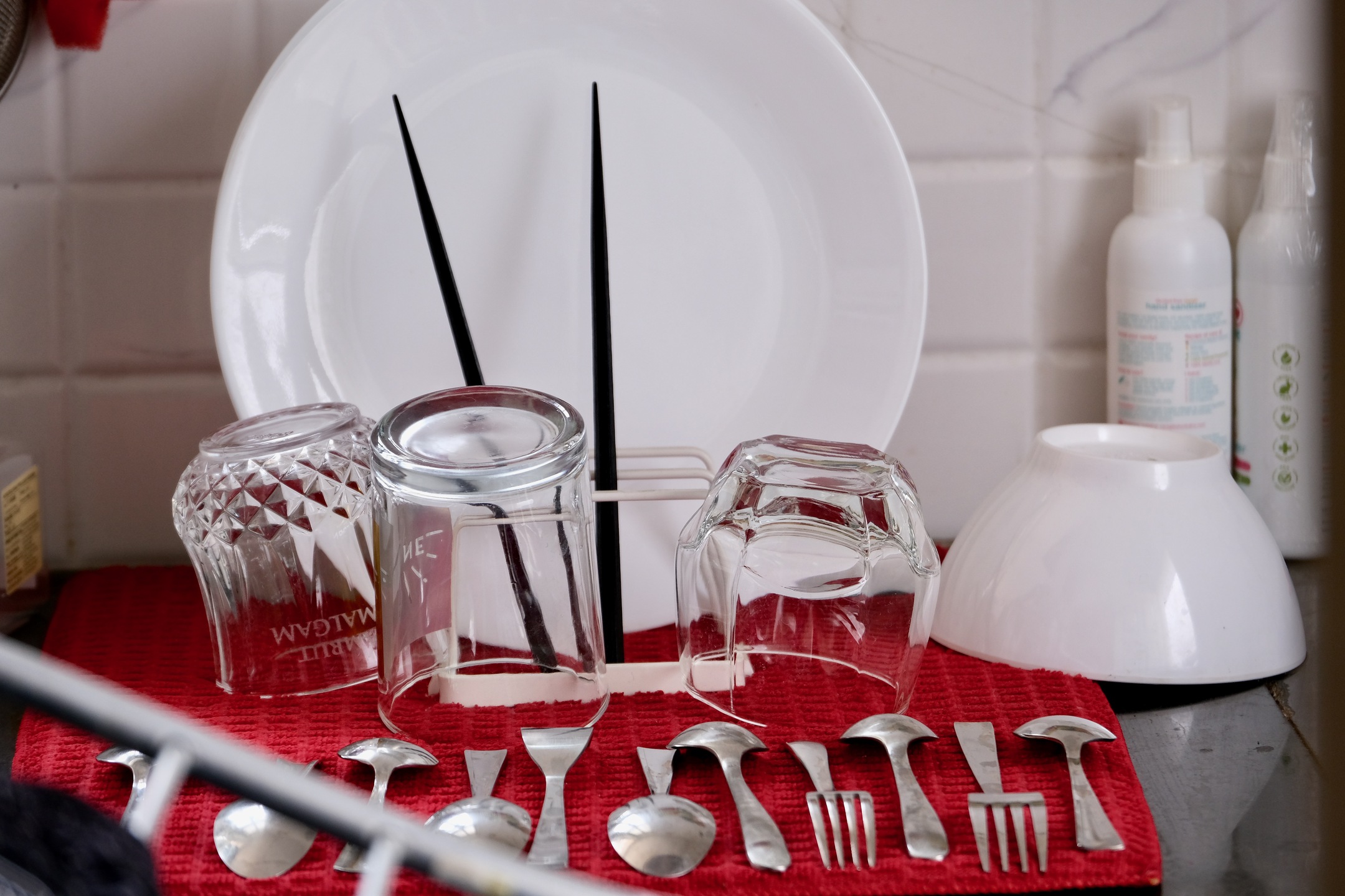 A close-up shot showing washed plates, chopsticks, spoons, forks, and glasses on a red drying mat.